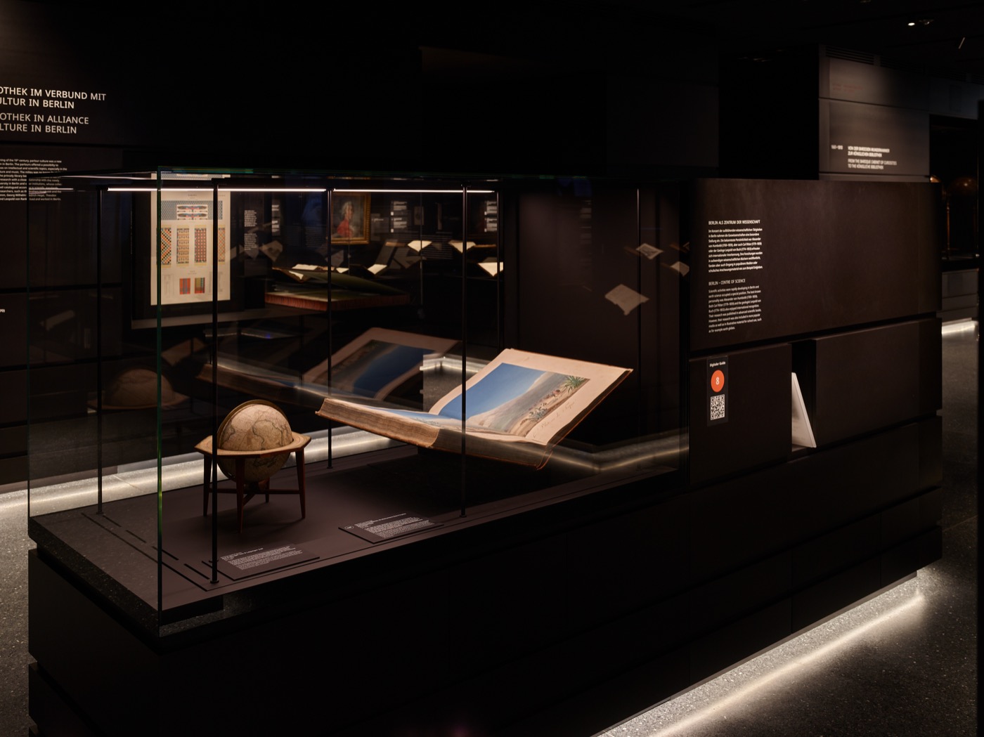 Dauerausstellungsbereich im Stabi-Kulturwerk mit schwarzen Vitrinenkörpern mit Sockelunterleuchtung und integrierter Vitrinenbeleuchtung, Globus in Vitrine und aufgeschlagenes Buch